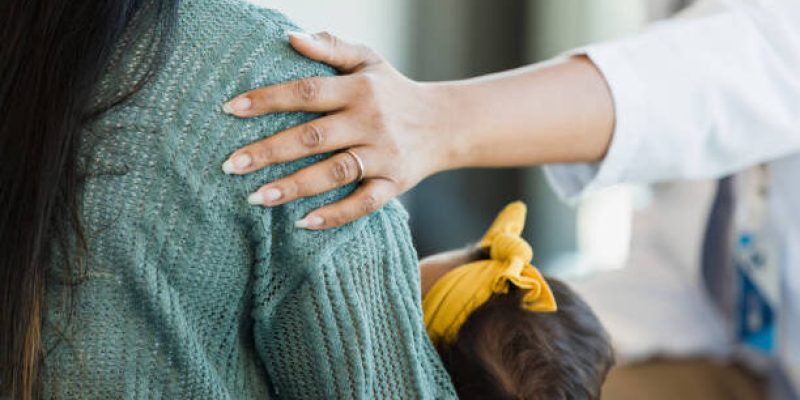 Unrecognizable person places hand on a mother's shoulder as she offers comfort and support.