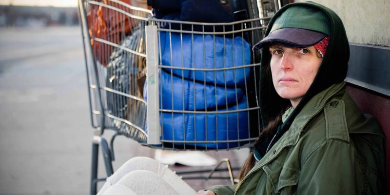 A homeless woman sitting on a sidewalk.