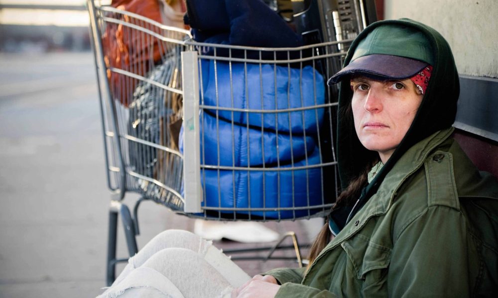 A homeless woman sitting on a sidewalk.